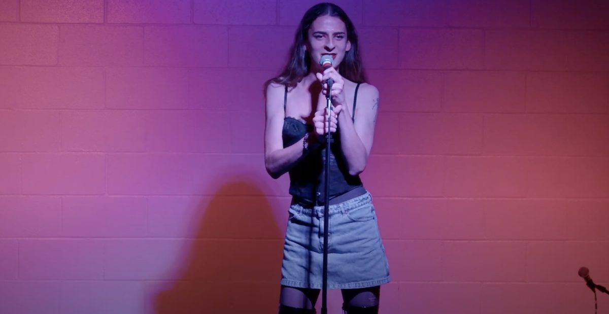 Performer singing at a mic stand against a pink wall