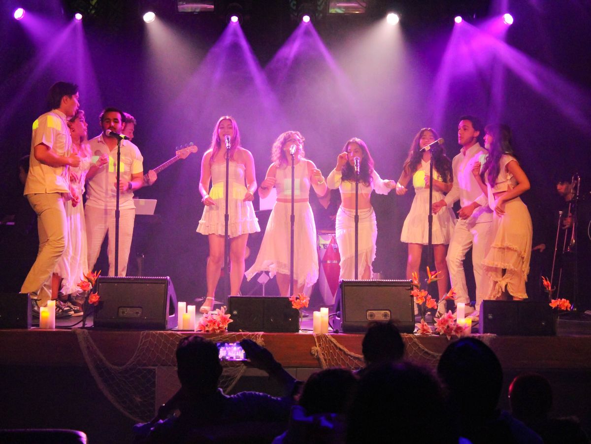 Full ensemble in white singing at a row of microphones