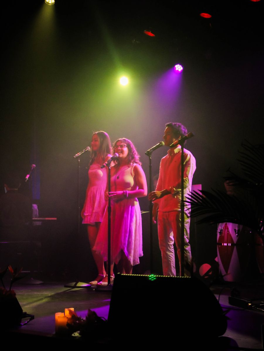 Singers in white under pink and green light