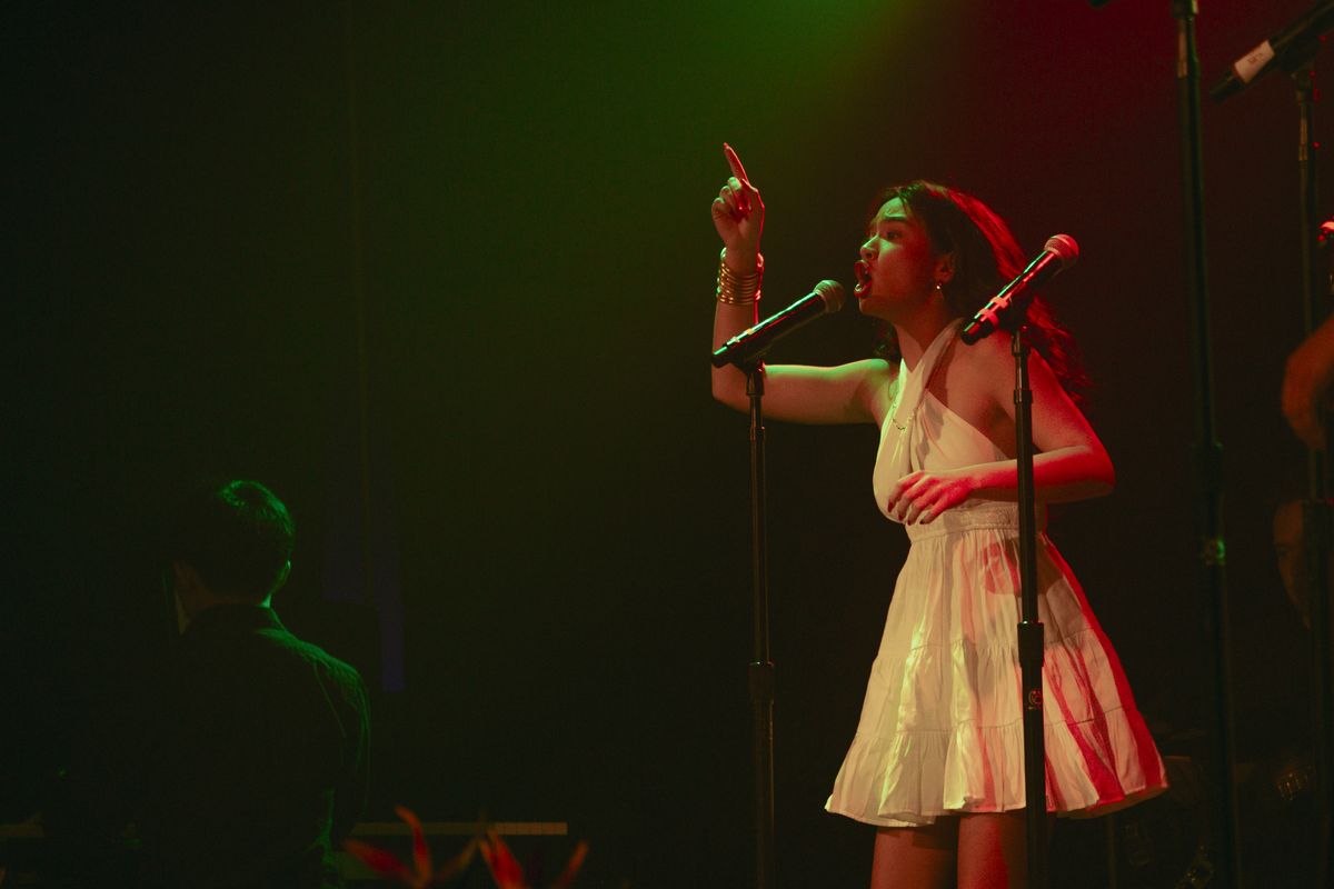 Singer in a white dress performing with one arm raised